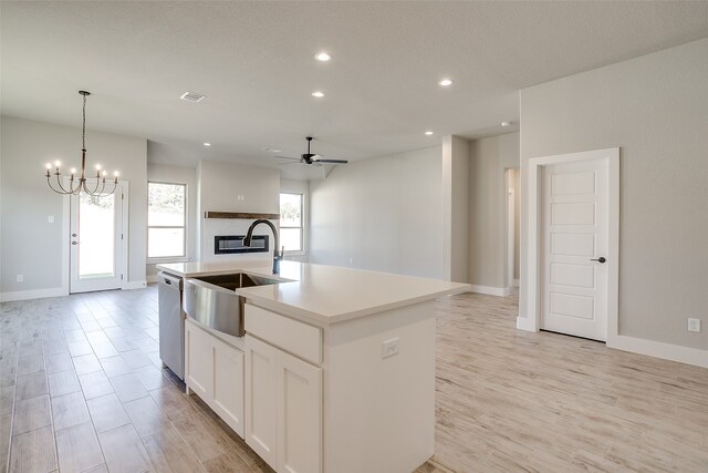 kitchen featuring a center island with sink, hanging light fixtures, sink, white cabinets, and stainless steel dishwasher