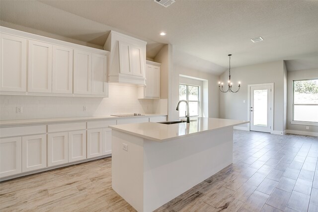 kitchen featuring white cabinets, hanging light fixtures, sink, a notable chandelier, and a kitchen island with sink