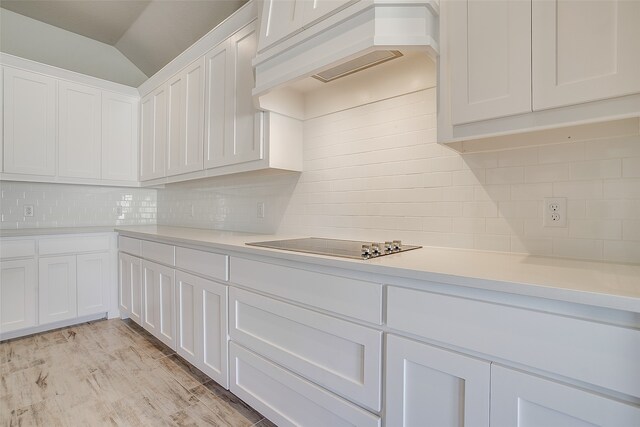 kitchen with white cabinetry, custom range hood, lofted ceiling, and tasteful backsplash