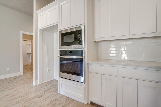 kitchen with a textured ceiling, tasteful backsplash, white cabinetry, light wood-type flooring, and appliances with stainless steel finishes