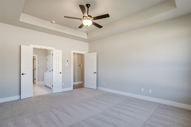 unfurnished bedroom featuring light carpet, ceiling fan, and a raised ceiling