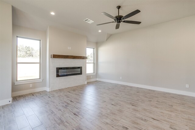 unfurnished living room with heating unit, light wood-type flooring, a tiled fireplace, and ceiling fan