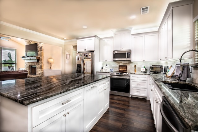 kitchen with appliances with stainless steel finishes, white cabinetry, dark hardwood / wood-style floors, dark stone counters, and a stone fireplace