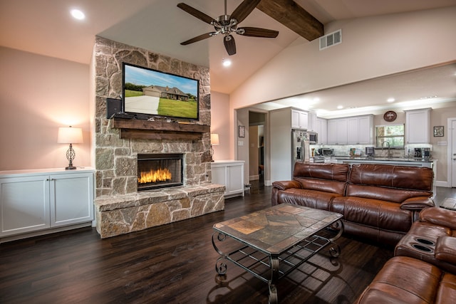 living room featuring beamed ceiling, sink, a stone fireplace, dark wood-type flooring, and ceiling fan