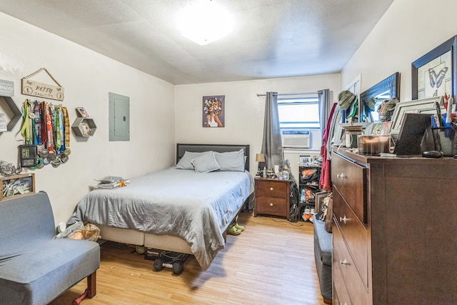 bedroom featuring electric panel, a textured ceiling, cooling unit, and light hardwood / wood-style floors