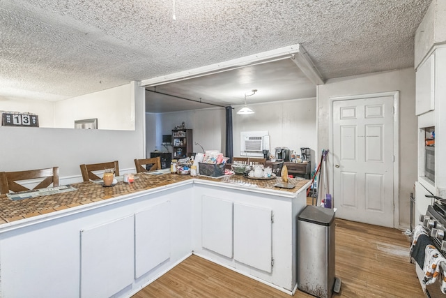 kitchen featuring light wood-type flooring, pendant lighting, a textured ceiling, kitchen peninsula, and white cabinets