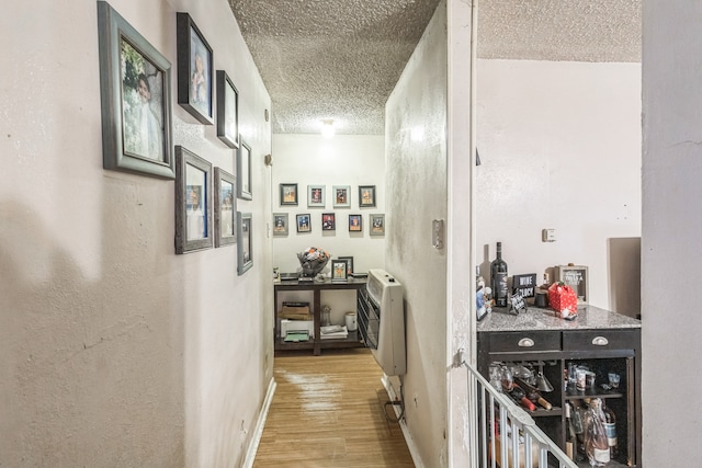 hallway with a textured ceiling, heating unit, and light hardwood / wood-style floors