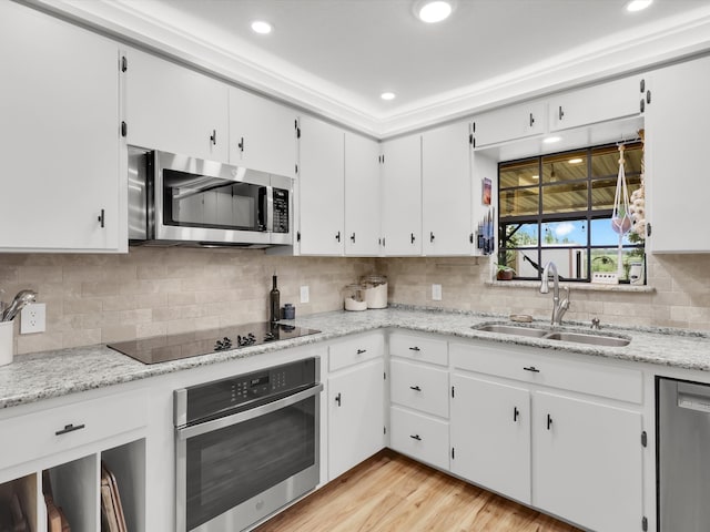 kitchen with light stone countertops, appliances with stainless steel finishes, sink, light hardwood / wood-style flooring, and white cabinetry