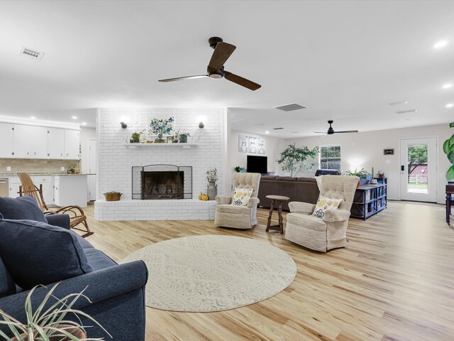 living room featuring ceiling fan, light hardwood / wood-style floors, and a brick fireplace