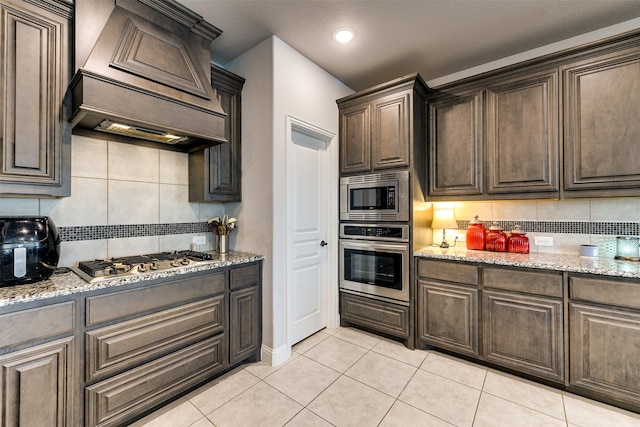 kitchen with appliances with stainless steel finishes, light stone counters, decorative backsplash, and premium range hood