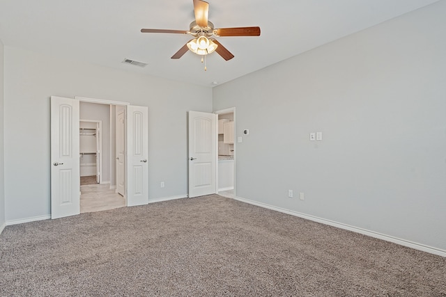 unfurnished bedroom featuring a walk in closet, ceiling fan, and light colored carpet