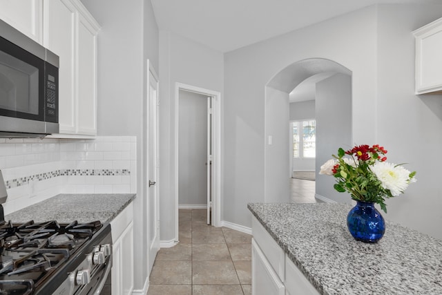 kitchen with light stone countertops, appliances with stainless steel finishes, light tile patterned floors, and white cabinetry