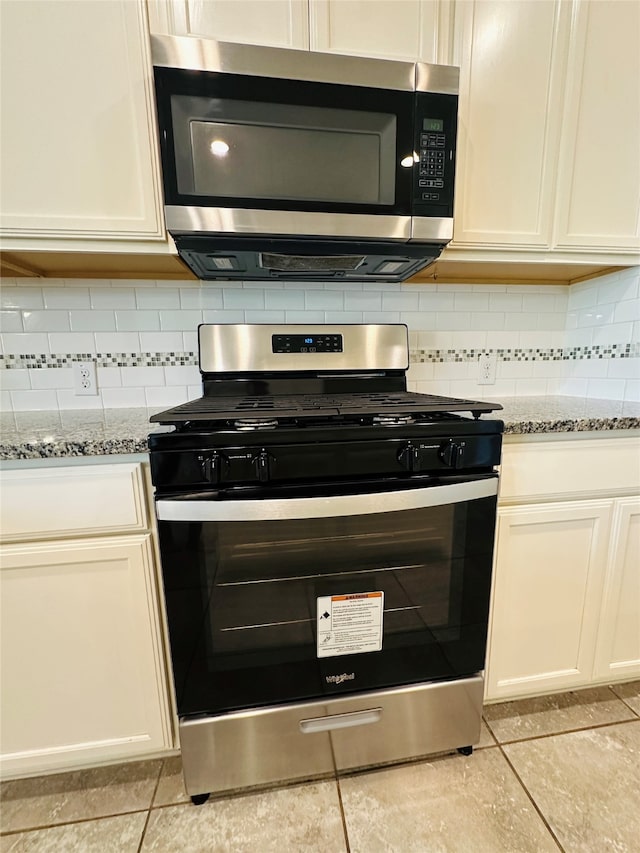 kitchen featuring light tile patterned flooring, light stone countertops, backsplash, and appliances with stainless steel finishes