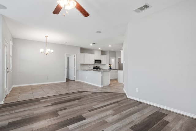 unfurnished living room with ceiling fan with notable chandelier and light wood-type flooring