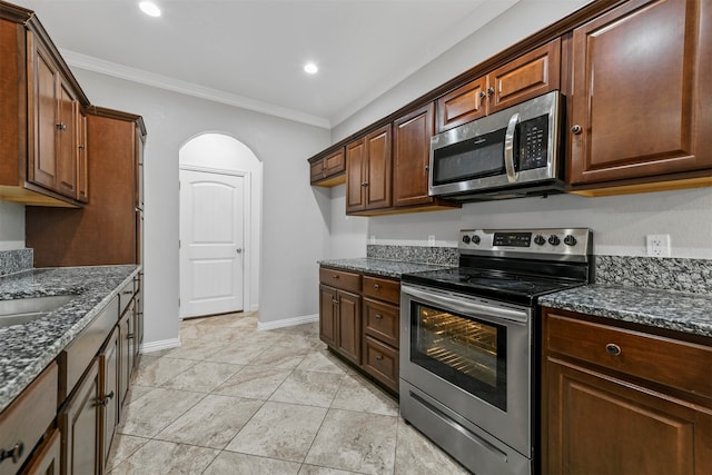 kitchen with light tile patterned floors, crown molding, appliances with stainless steel finishes, and dark stone counters