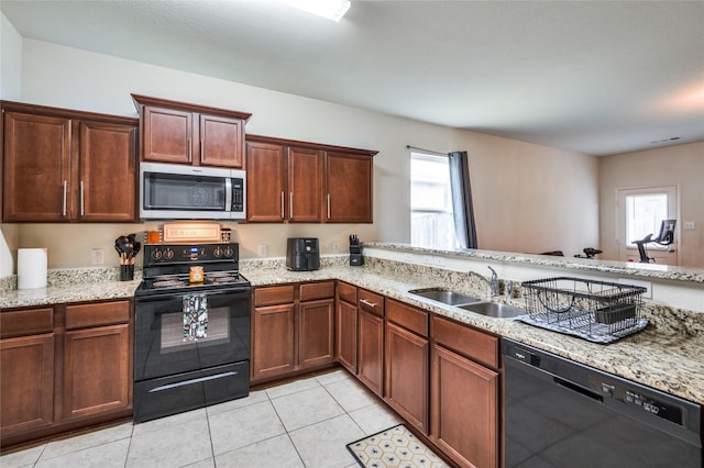 kitchen with a sink, light stone counters, black appliances, and a wealth of natural light