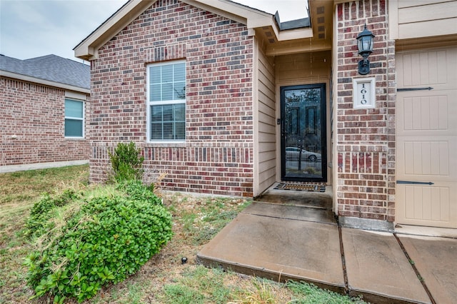 view of exterior entry featuring brick siding and an attached garage