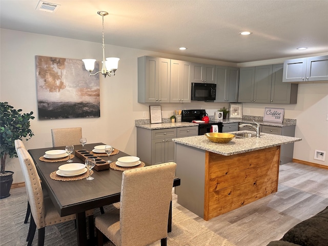 kitchen with light stone counters, pendant lighting, gray cabinets, black appliances, and light hardwood / wood-style flooring