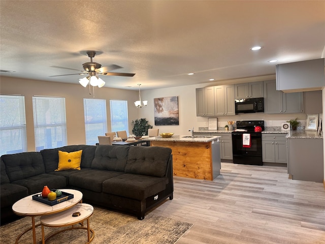 living room with light hardwood / wood-style flooring, a textured ceiling, ceiling fan with notable chandelier, and sink