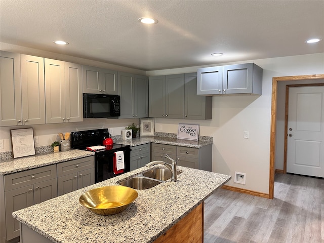 kitchen with black appliances, sink, light hardwood / wood-style flooring, and light stone counters