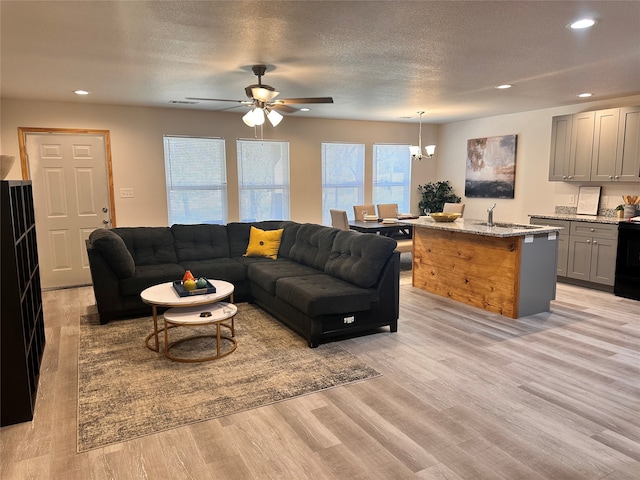 living room with a textured ceiling, ceiling fan with notable chandelier, sink, and light hardwood / wood-style floors