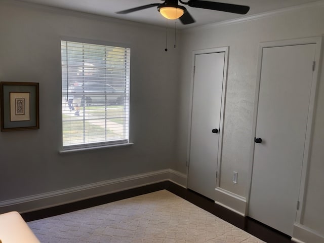 unfurnished bedroom featuring crown molding, hardwood / wood-style flooring, multiple closets, and ceiling fan