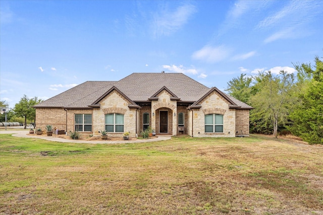 french country inspired facade with a shingled roof and a front lawn