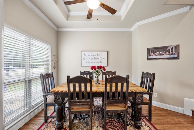 dining area featuring wood finished floors, a ceiling fan, baseboards, ornamental molding, and a raised ceiling