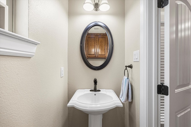 bathroom featuring an inviting chandelier, a sink, and a textured wall