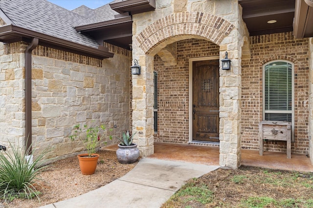 doorway to property featuring stone siding, a shingled roof, and brick siding