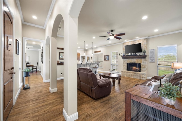 living room featuring dark wood-style floors, ornamental molding, a fireplace, and arched walkways