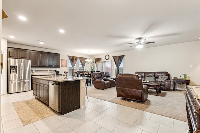 kitchen with dark brown cabinetry, appliances with stainless steel finishes, an island with sink, and light carpet