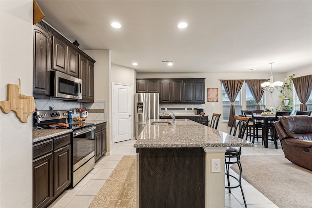 kitchen with tasteful backsplash, appliances with stainless steel finishes, a center island with sink, and light tile patterned floors