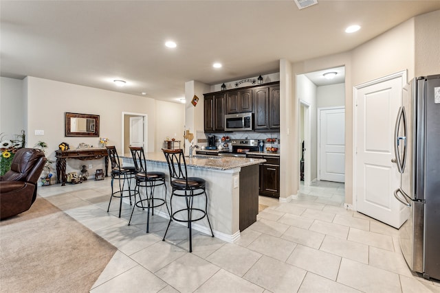 kitchen with light tile patterned floors, sink, a breakfast bar area, appliances with stainless steel finishes, and a center island with sink