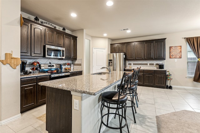 kitchen with stainless steel appliances, an island with sink, and dark brown cabinets