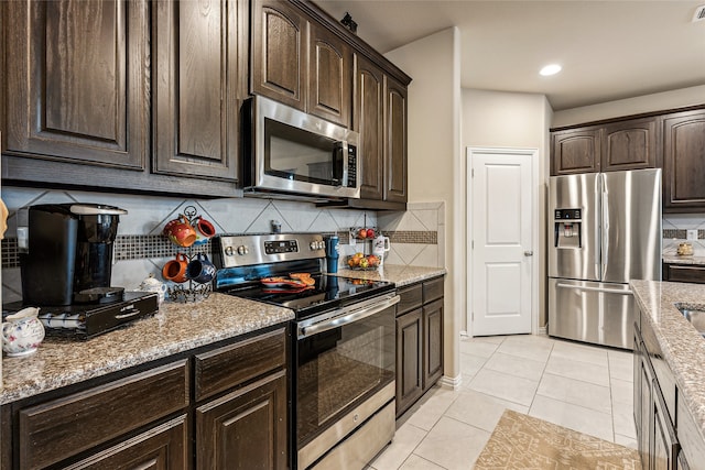 kitchen featuring dark brown cabinetry, tasteful backsplash, light tile patterned floors, stainless steel appliances, and light stone countertops