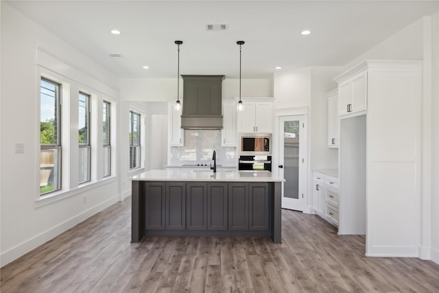 kitchen featuring white cabinets, light hardwood / wood-style flooring, stainless steel appliances, premium range hood, and an island with sink