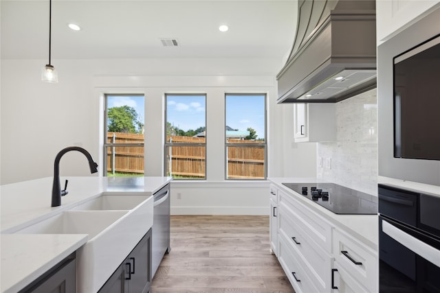 kitchen with custom exhaust hood, white cabinetry, light hardwood / wood-style flooring, black appliances, and hanging light fixtures