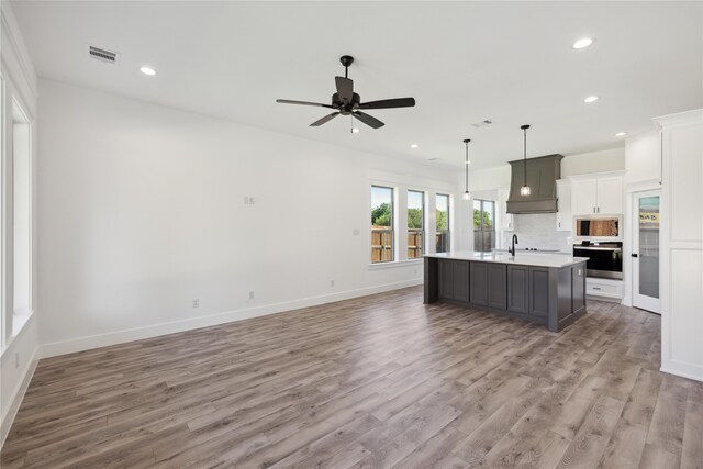 kitchen with a center island with sink, hardwood / wood-style floors, appliances with stainless steel finishes, white cabinetry, and ceiling fan