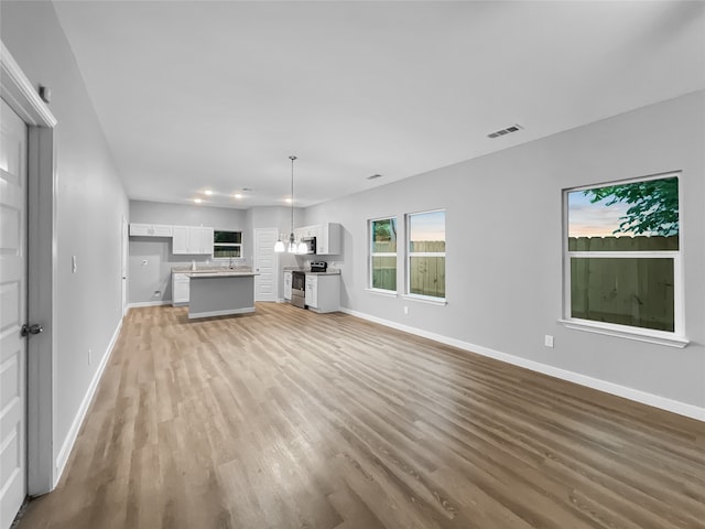 unfurnished living room with light wood-type flooring and an inviting chandelier