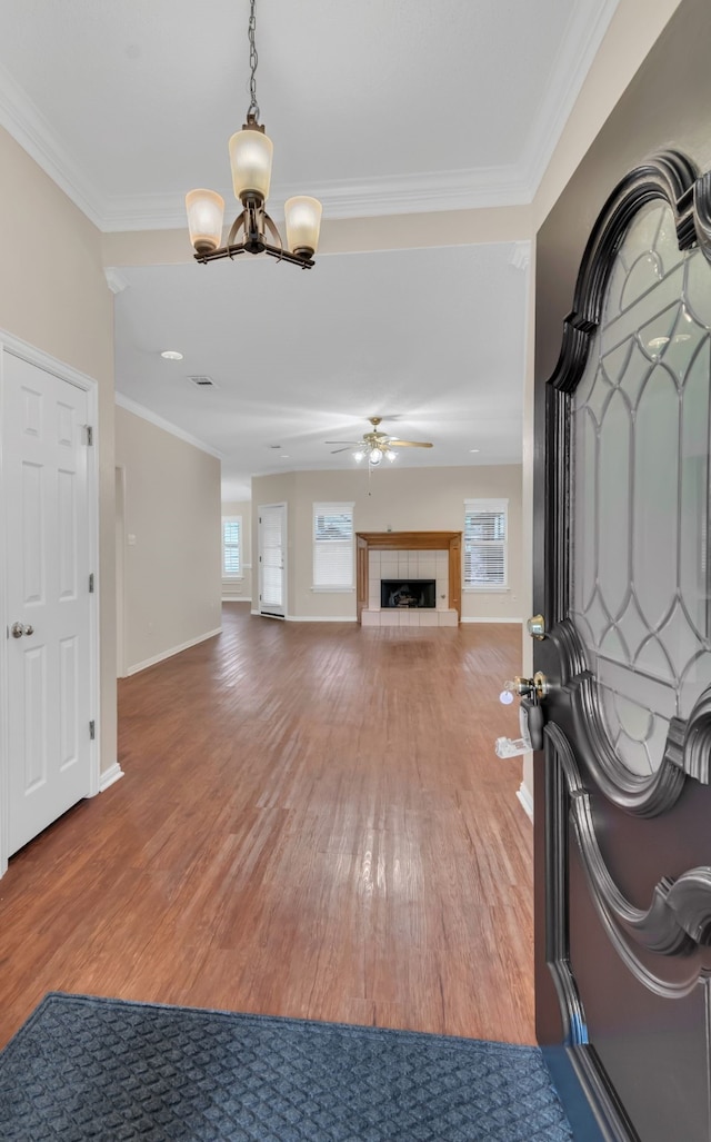 unfurnished living room featuring crown molding, ceiling fan with notable chandelier, hardwood / wood-style floors, and a tile fireplace