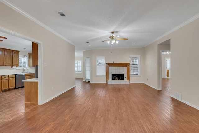 unfurnished living room featuring a tiled fireplace, crown molding, ceiling fan, and light hardwood / wood-style floors