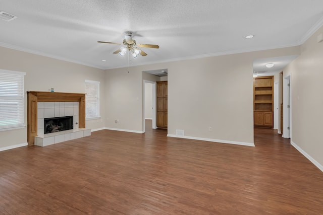 unfurnished living room featuring a tiled fireplace, ornamental molding, a textured ceiling, wood-type flooring, and ceiling fan