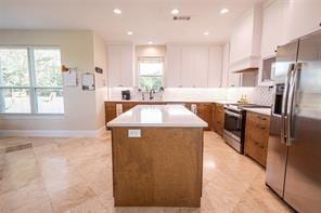 kitchen featuring tasteful backsplash, a kitchen island, custom range hood, appliances with stainless steel finishes, and brown cabinetry