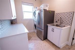 clothes washing area featuring a sink, stacked washer / drying machine, laundry area, and light tile patterned floors