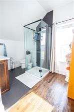 full bath featuring toilet, a stall shower, wood finished floors, vanity, and vaulted ceiling