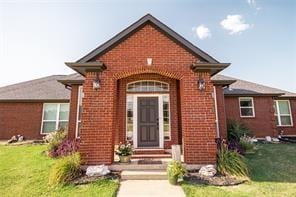 view of exterior entry with brick siding and a yard