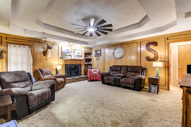 carpeted living room featuring a tray ceiling, ceiling fan, and a brick fireplace