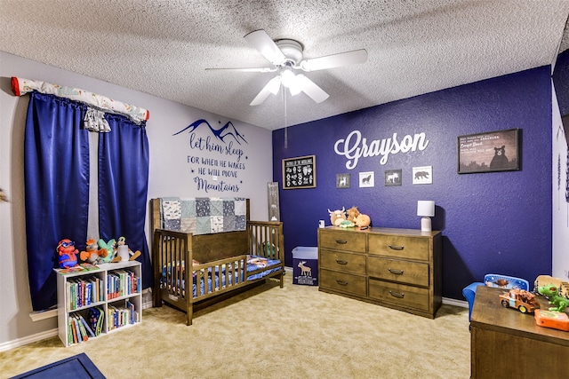 carpeted bedroom with ceiling fan, a crib, and a textured ceiling