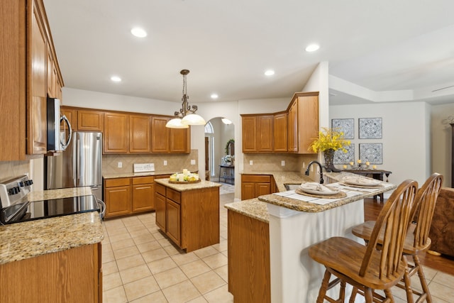 kitchen featuring a kitchen breakfast bar, pendant lighting, appliances with stainless steel finishes, a center island, and kitchen peninsula